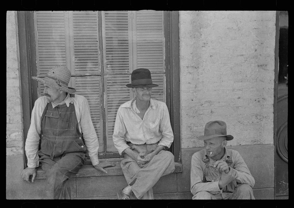 Old black and white photo of workers sitting on a window sill.