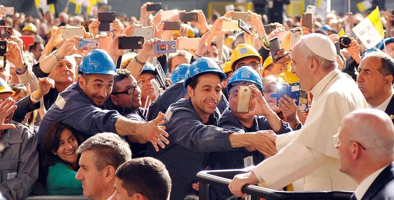 A crowd of workers in hard hats shake hands with the Pope.