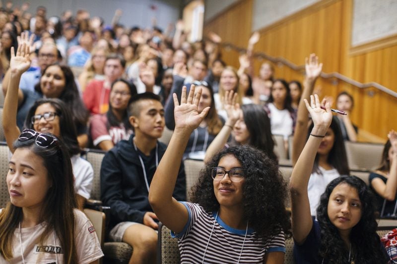 Students in a classroom raise hands.