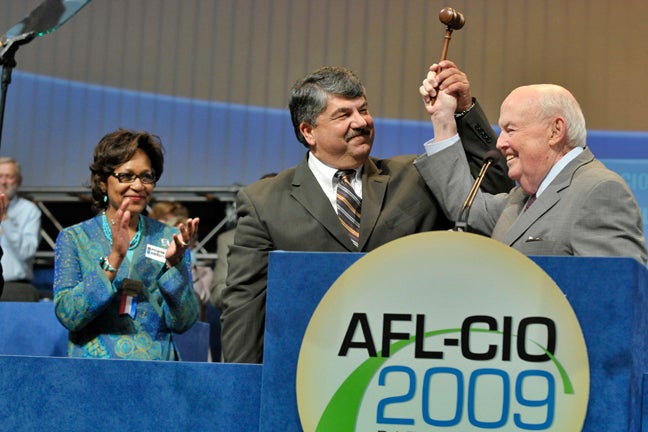 Richard Trumka and John Sweeney stand in front of a podium holding a gavel. The podium has a sign with the words 