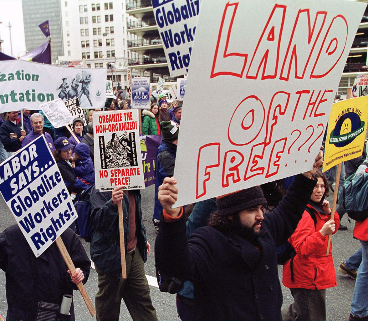Protesters holding signs with slogans including "Land of the Free???," "Labor Says... Globalize Workers Rights!," and "Organize the Non-Organized! No Separate Peace!"