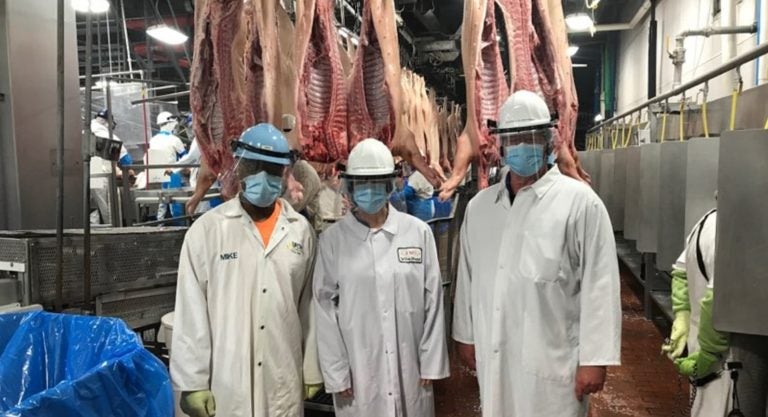 Meatpacking workers wearing masks and face shields pose for a picture in a factory.