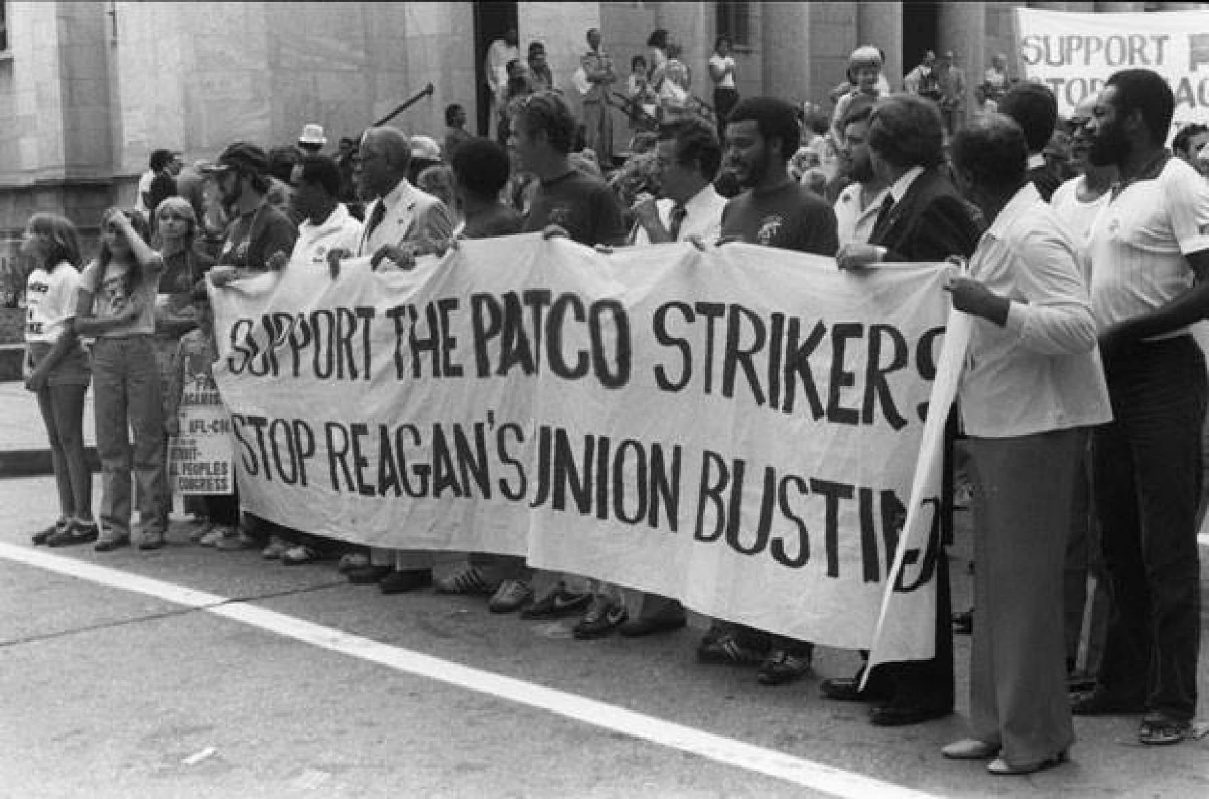Old-looking black and white photograph of protesters holding a banner that says 