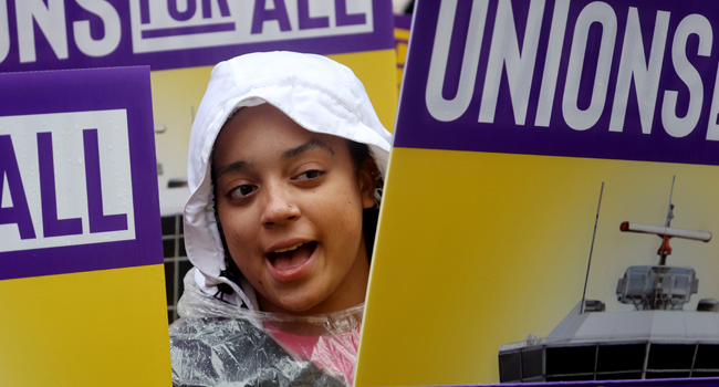 Child's head peaks out behind protest signs with the phrase "Unions for All."